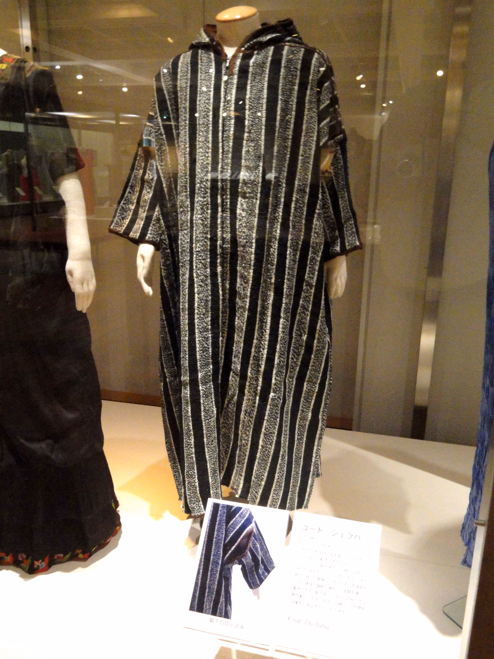 A striped hooded djellaba on a museum mannequin, the pointed hood lying back against the shoulders.
