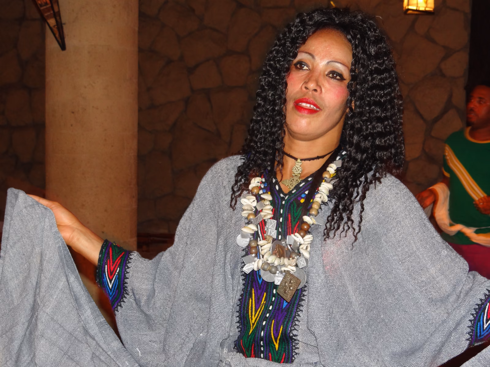A woman dances in a white habesha kemis edged with a woven coloured border, wearing layered necklaces.