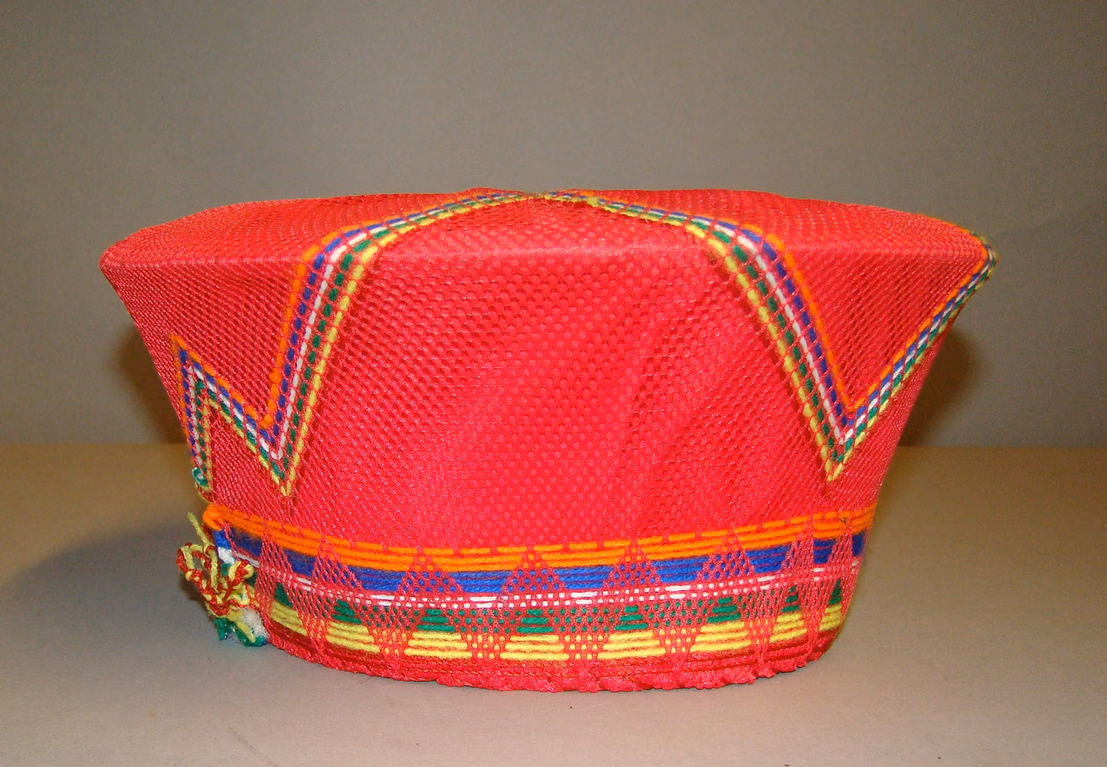 A wide red isicholo, flared like a shallow bowl, banded around its base with fine multicoloured beadwork.