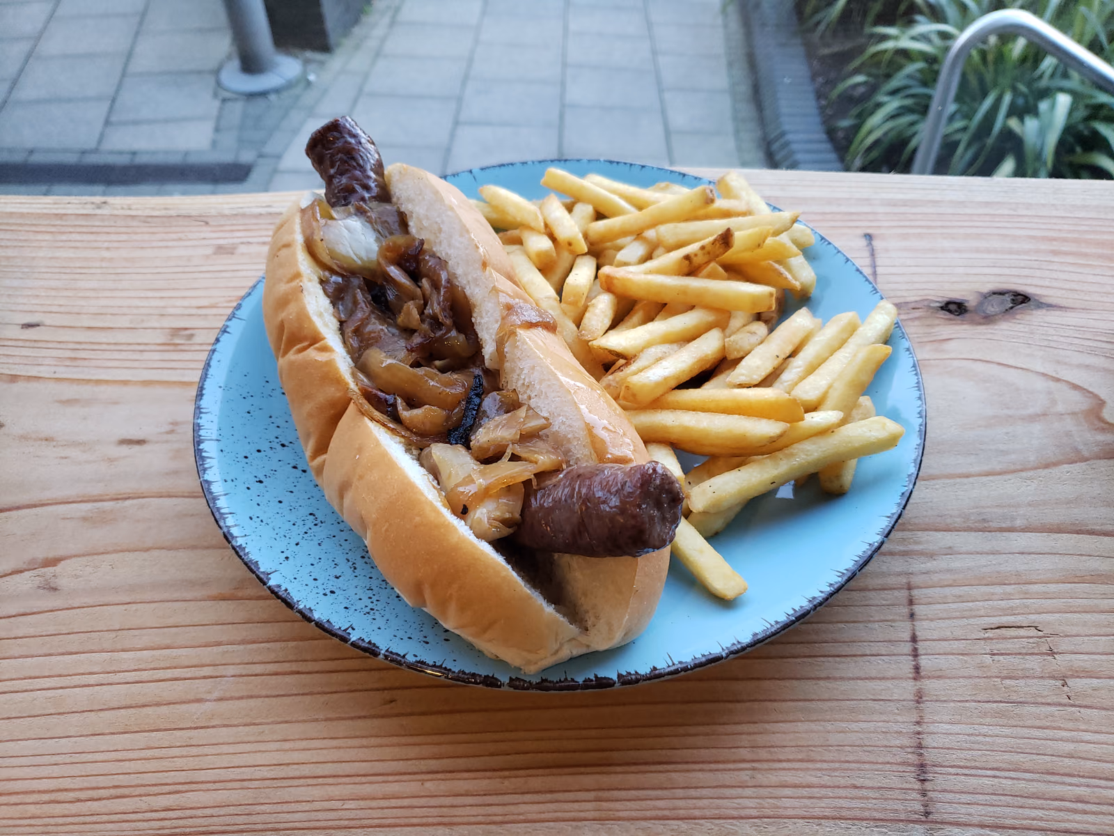 A boerewors roll: a coiled grilled sausage in a bread roll, served with chips on a blue plate.