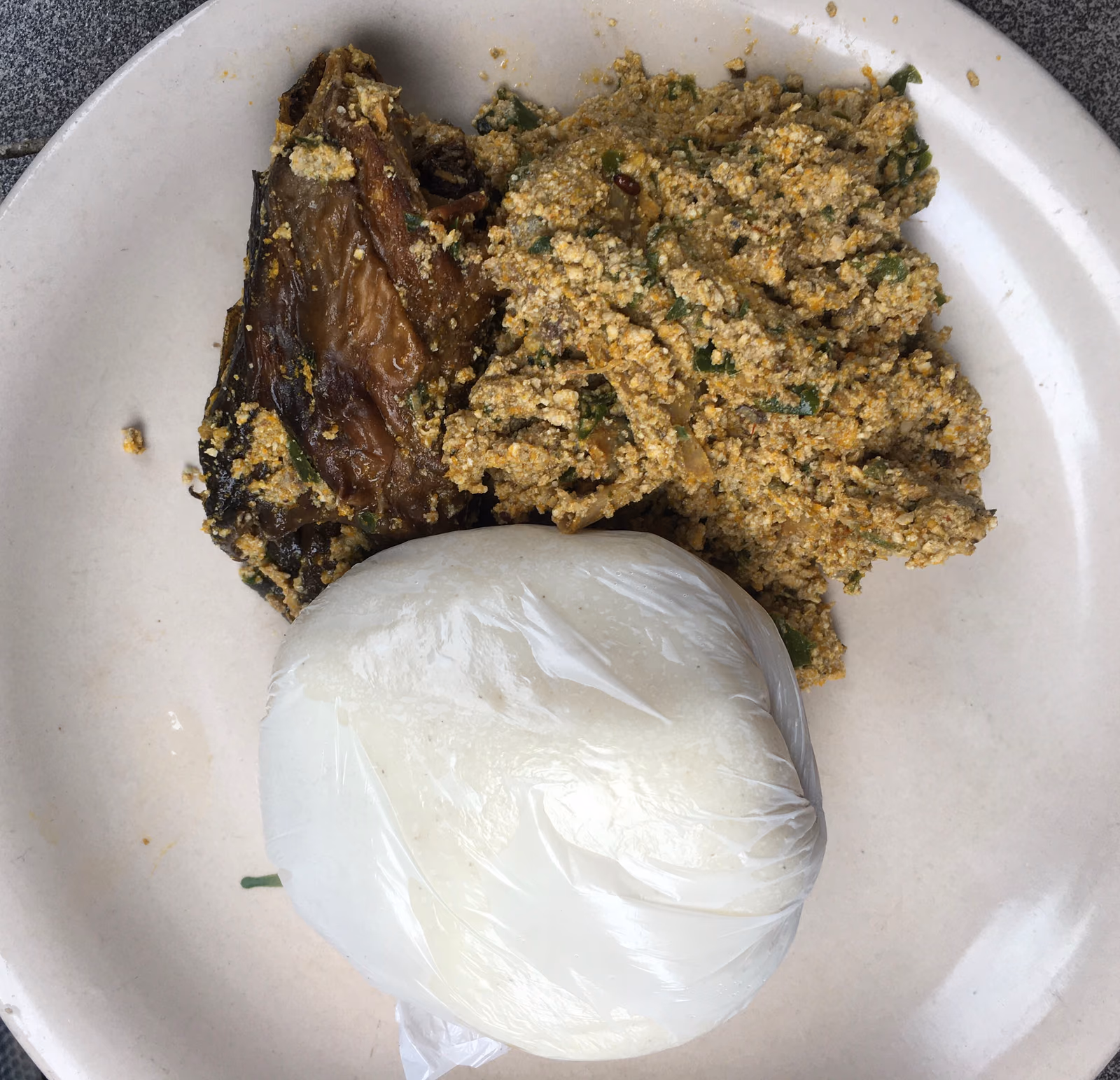 A plate of dark green egusi soup beside a smooth white ball of swallow.