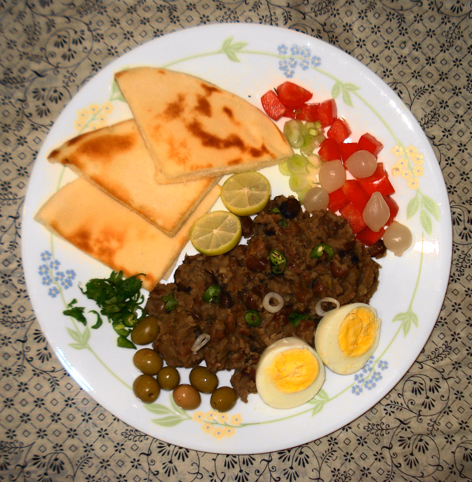 A plate of stewed brown fava beans with flatbread, boiled egg and chopped salad.