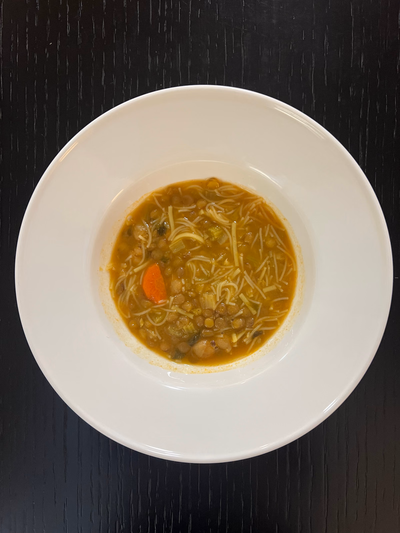 A white bowl of harira, a thin tomato broth with pulses, vermicelli and carrot.