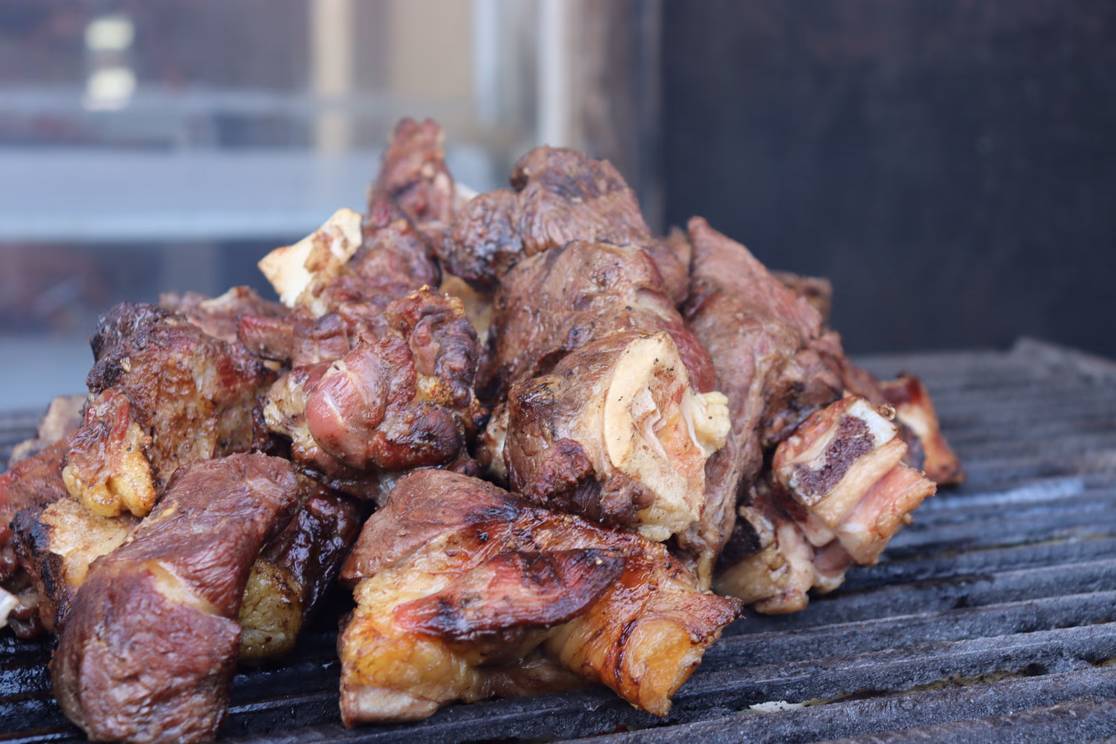 A plate heaped with pieces of roasted meat, browned and charred at the edges, cut from the bone.