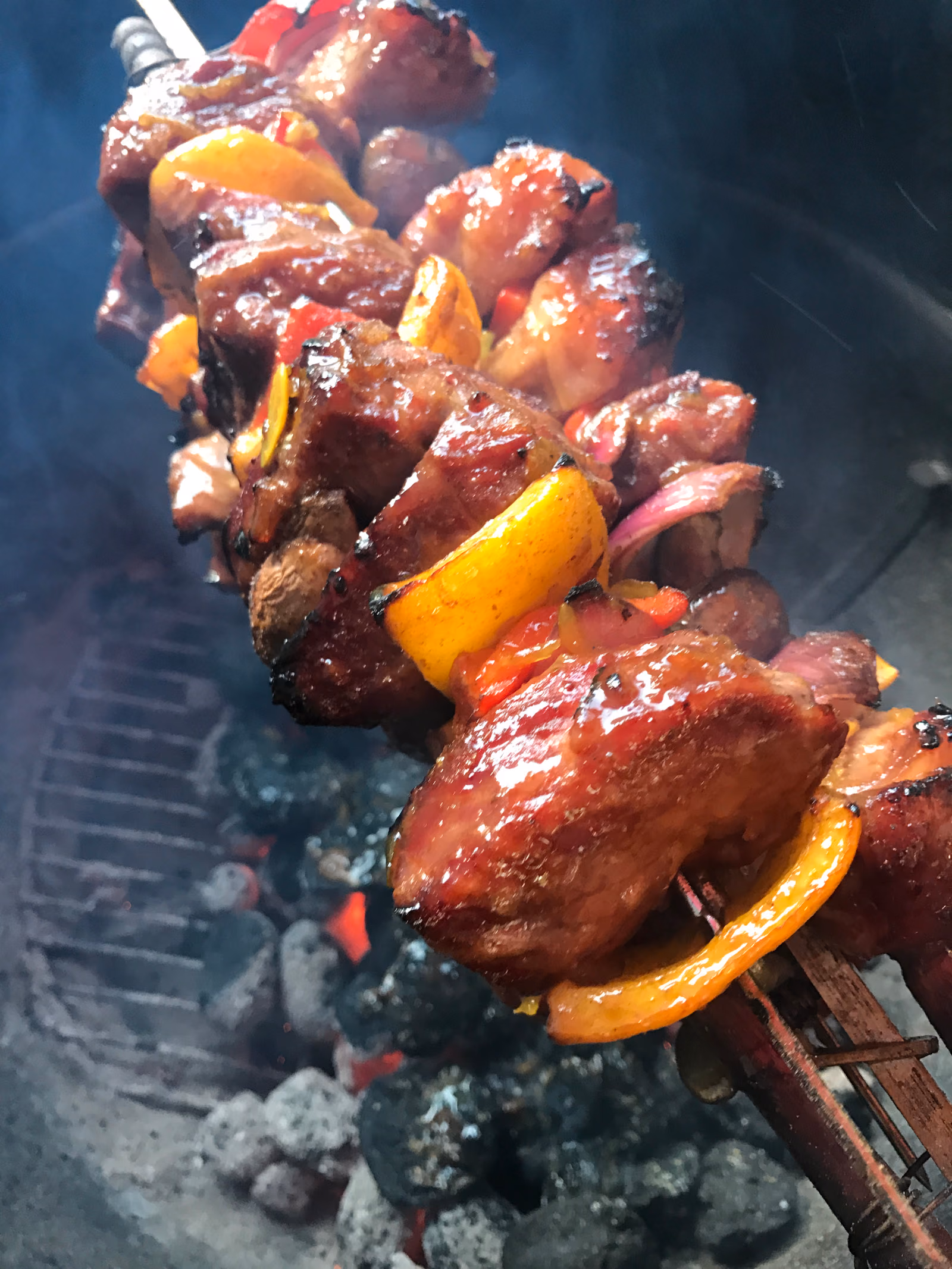 Skewers of marinated meat threaded with onion and dried apricot, browning over the coals of a braai.