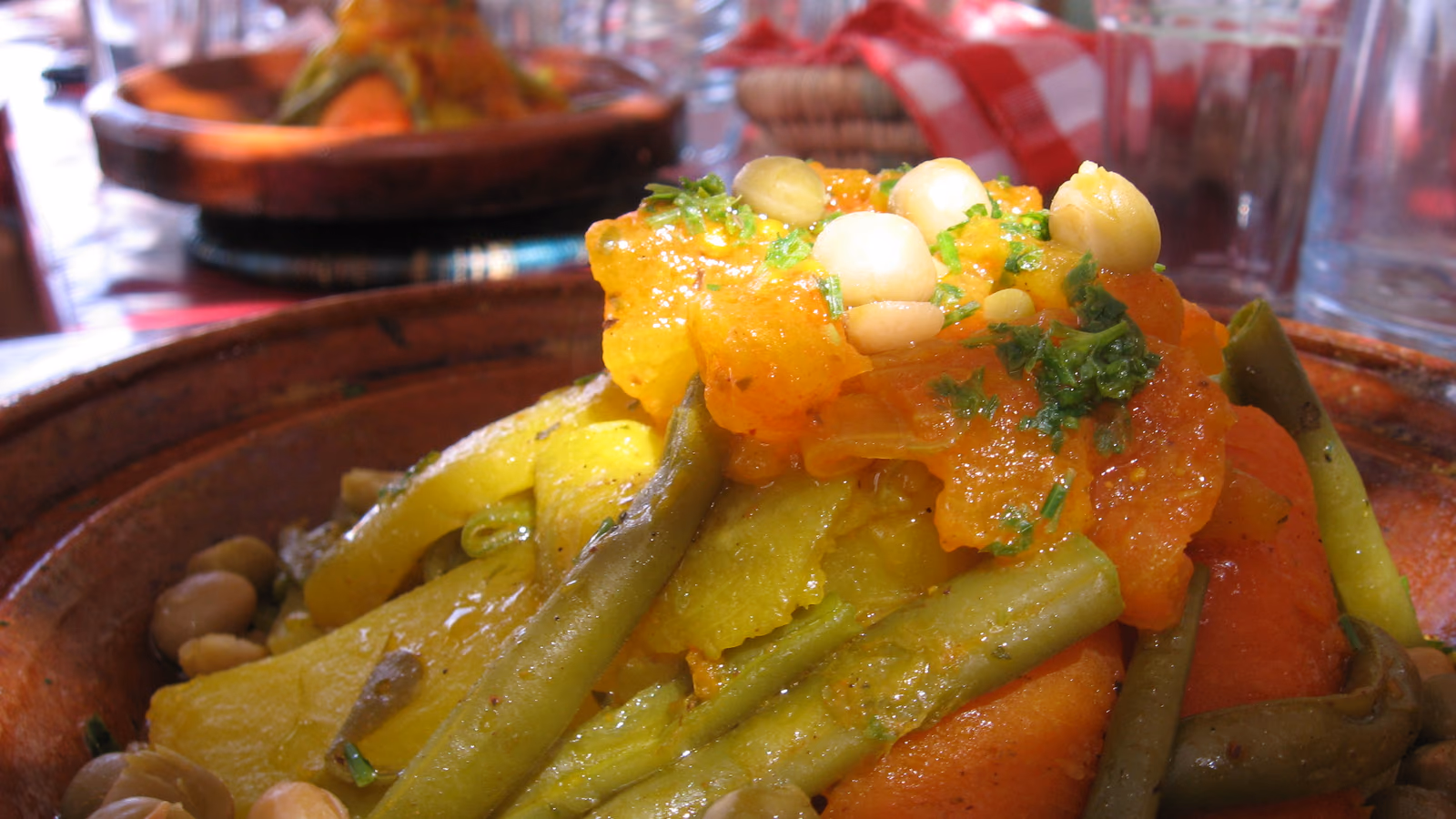 A close view of a vegetable tagine in its glazed clay dish: green beans, carrot, courgette and chickpeas under a spoonful of caramelised tomato and onion.