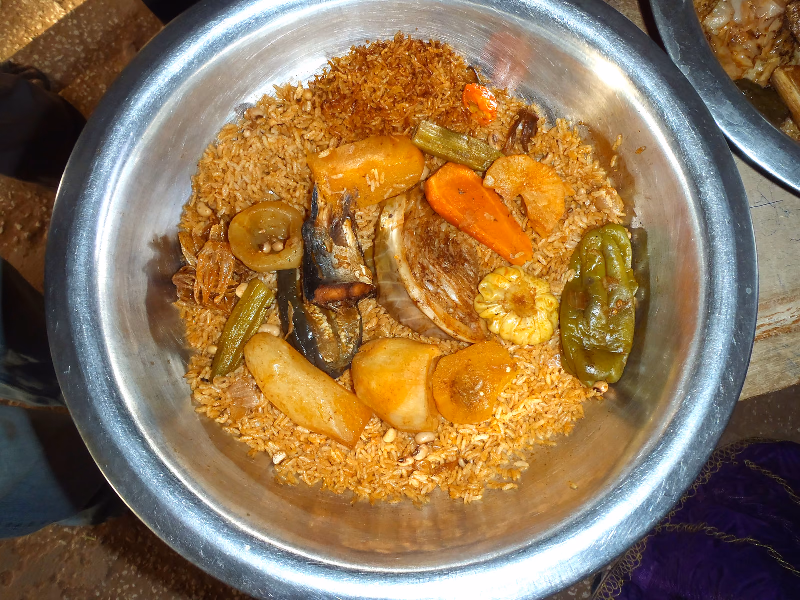 A wide metal dish of rice cooked orange in tomato, with a piece of fish and whole vegetables set into it.
