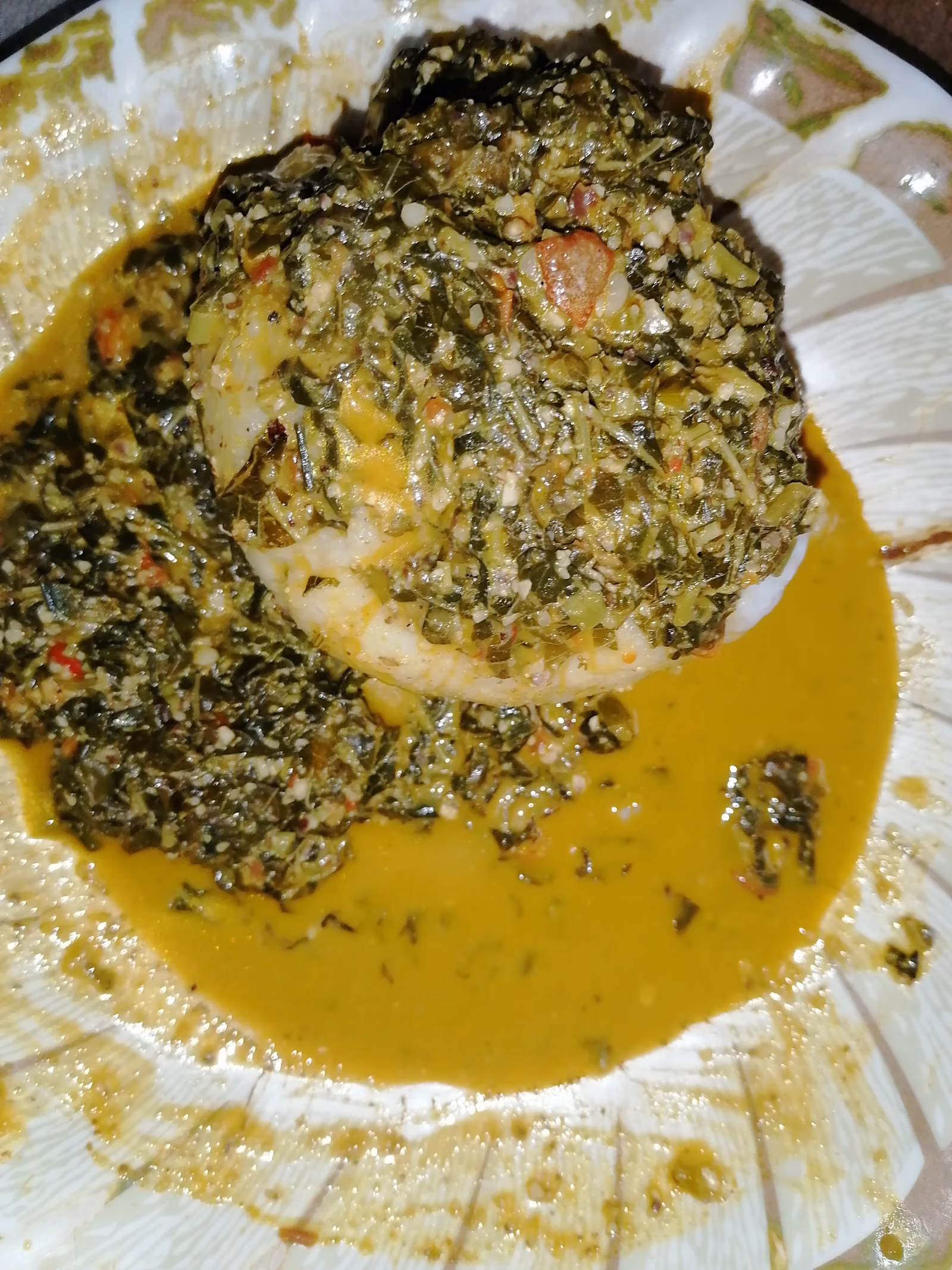 A smooth white mound of pounded rice set in a bowl of golden-green soup thick with chopped leaves.